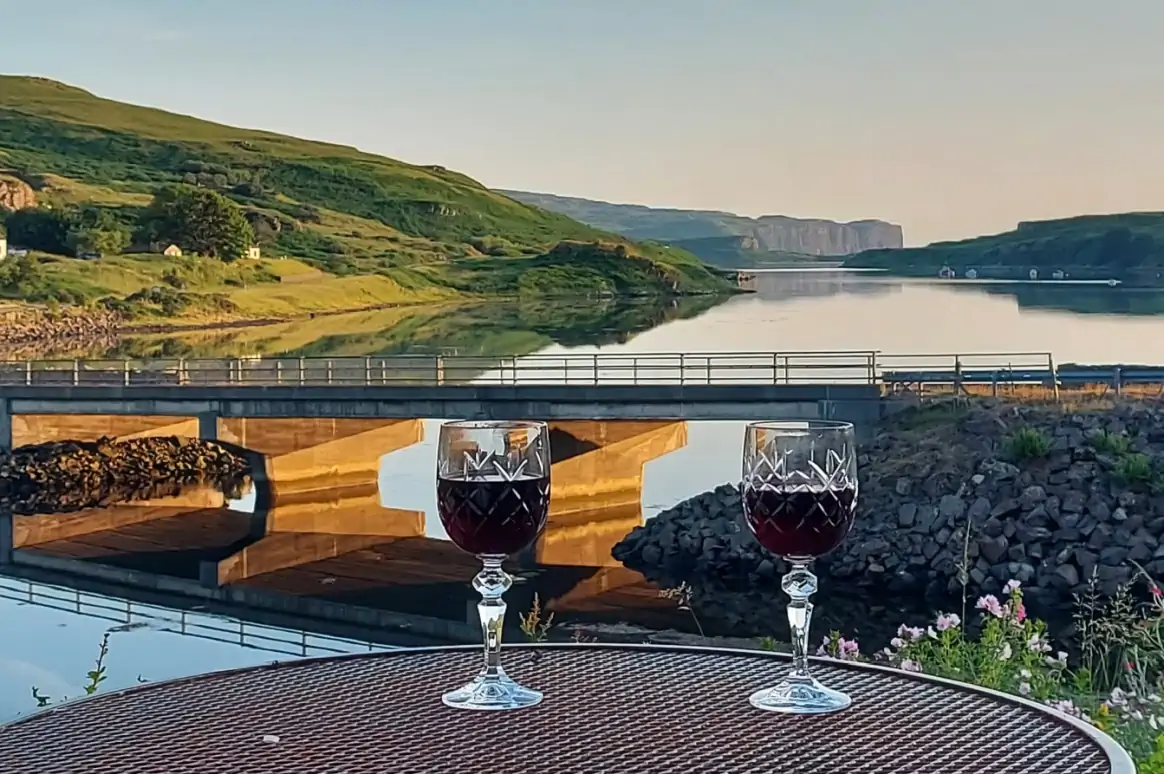 Looking out over Loch Baeg in sunset with 2 glasses of wine in the foreground on a table.